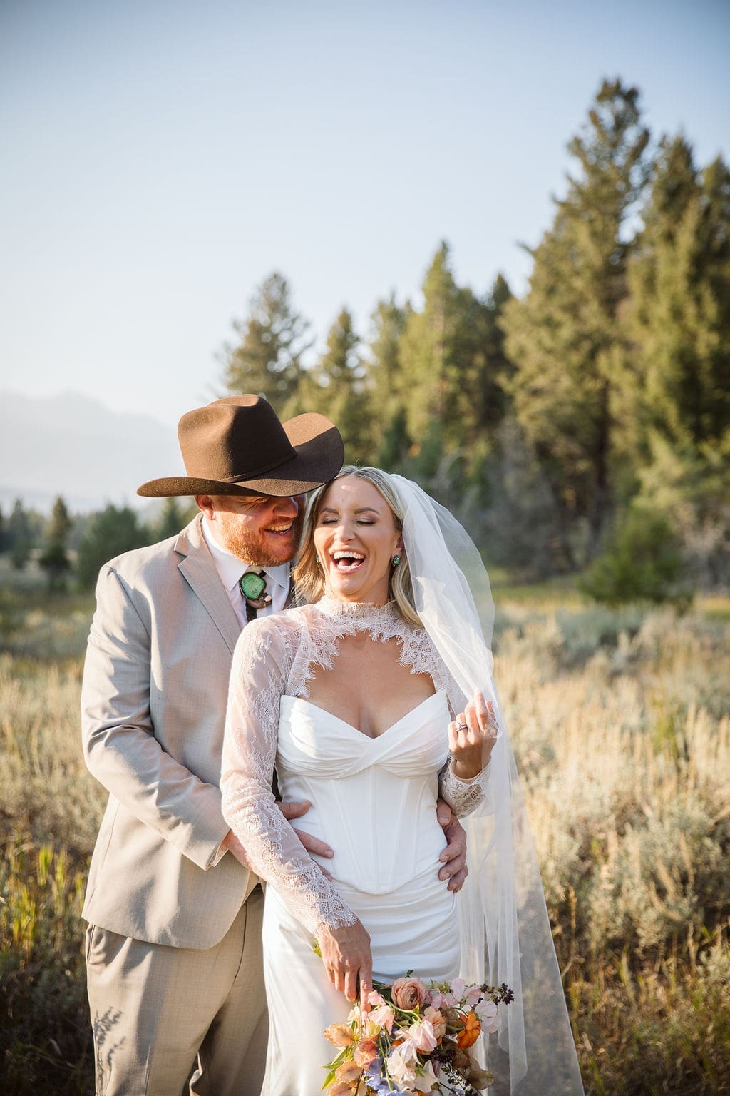 Couple in wedding attire laughing in golden field during luxury Bozeman wedding. 