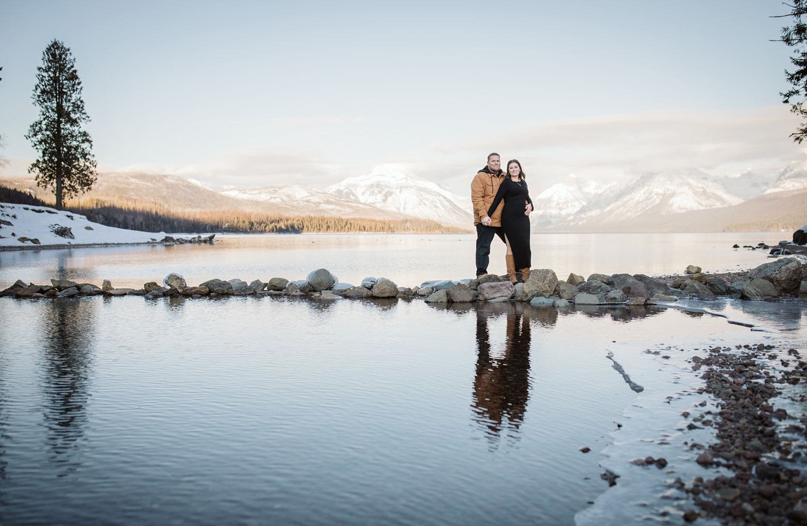 Couple standing on rocks in river during their winter Glacier National Park engagement photos. 