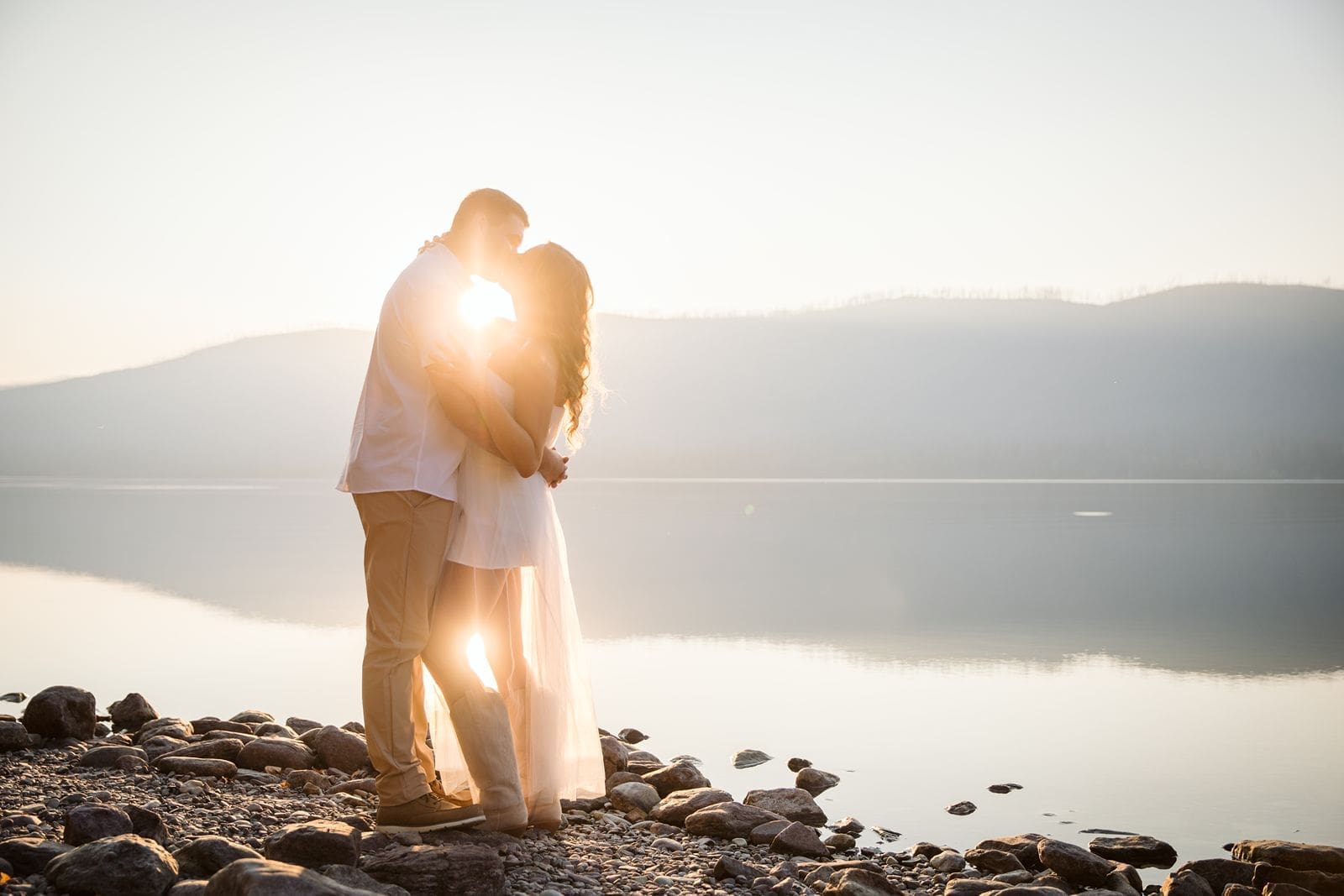 Couple kissing in front of lake at sunset