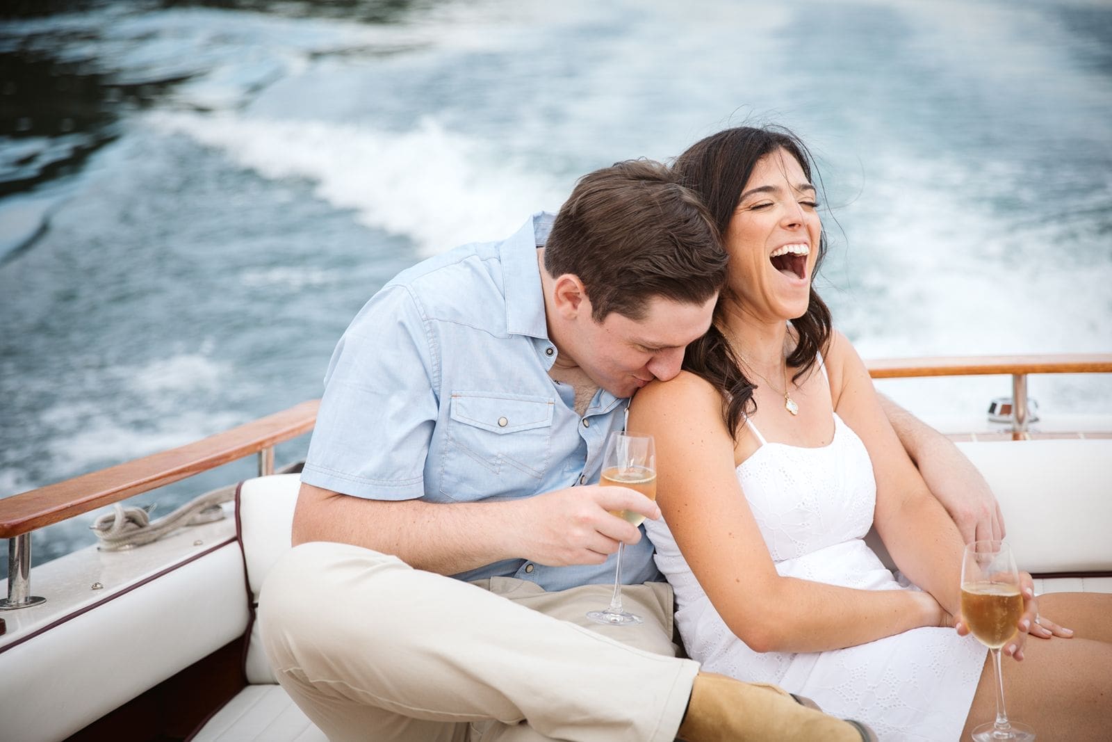 Couple laughing on boat drinking champagne during engagement photos with a Montana Wedding Photographer