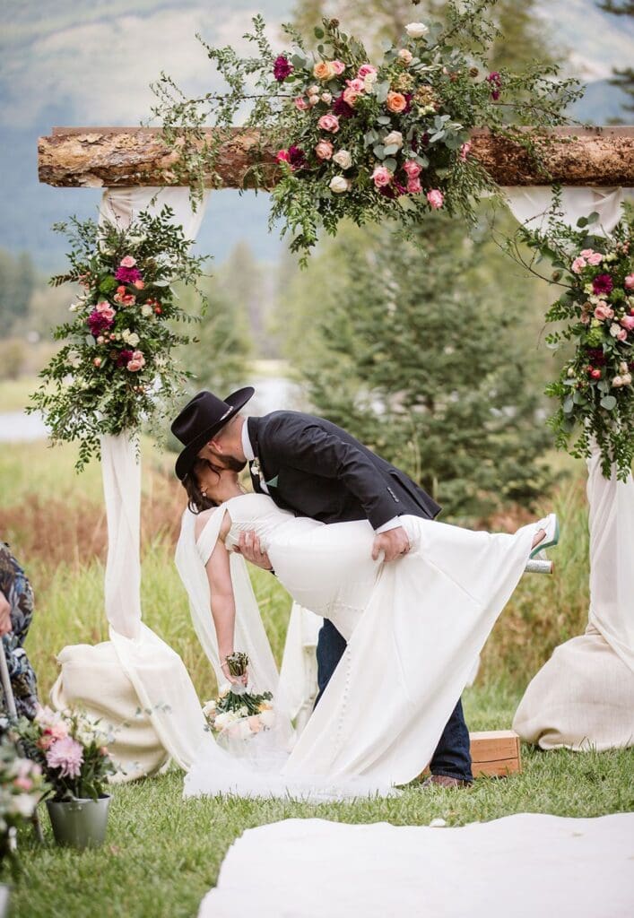 First dip kiss under floral arch during Bigfork wedding ceremony